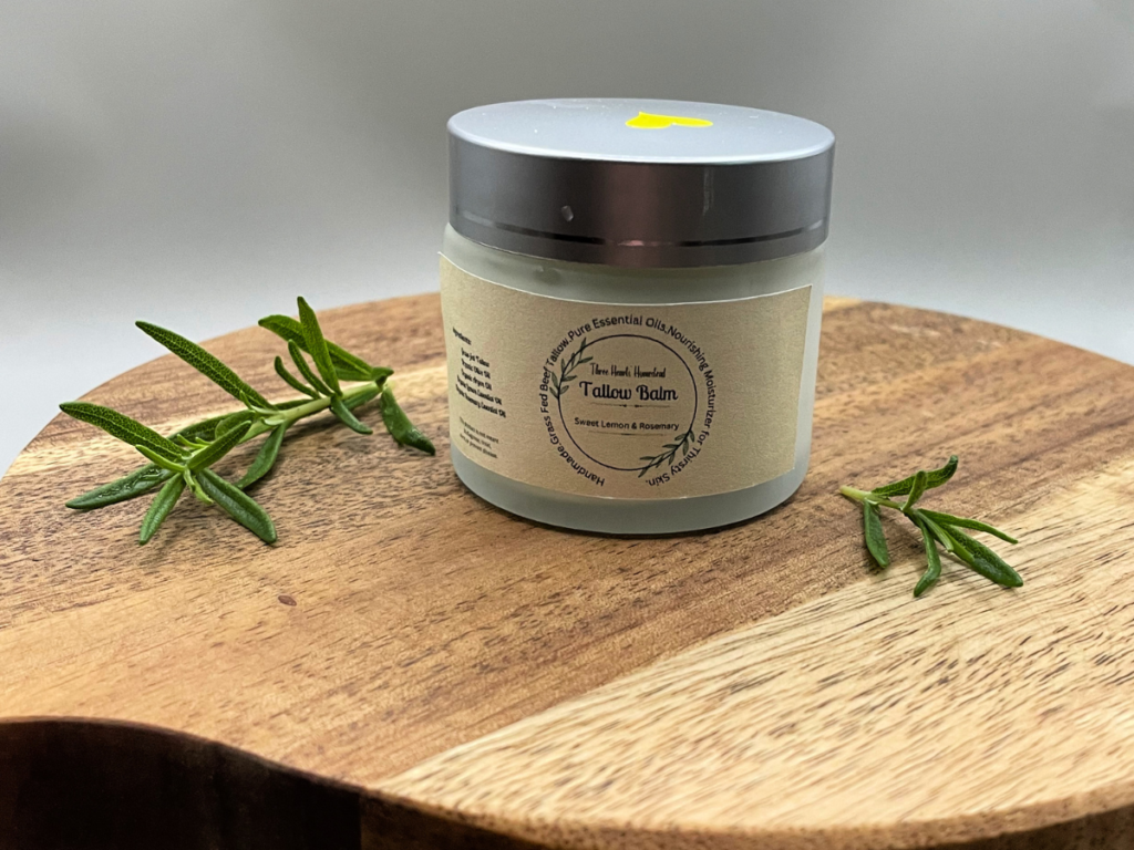 Picture of a jar of tallow balm on a wooden stand surrounded by rosemary sprigs.