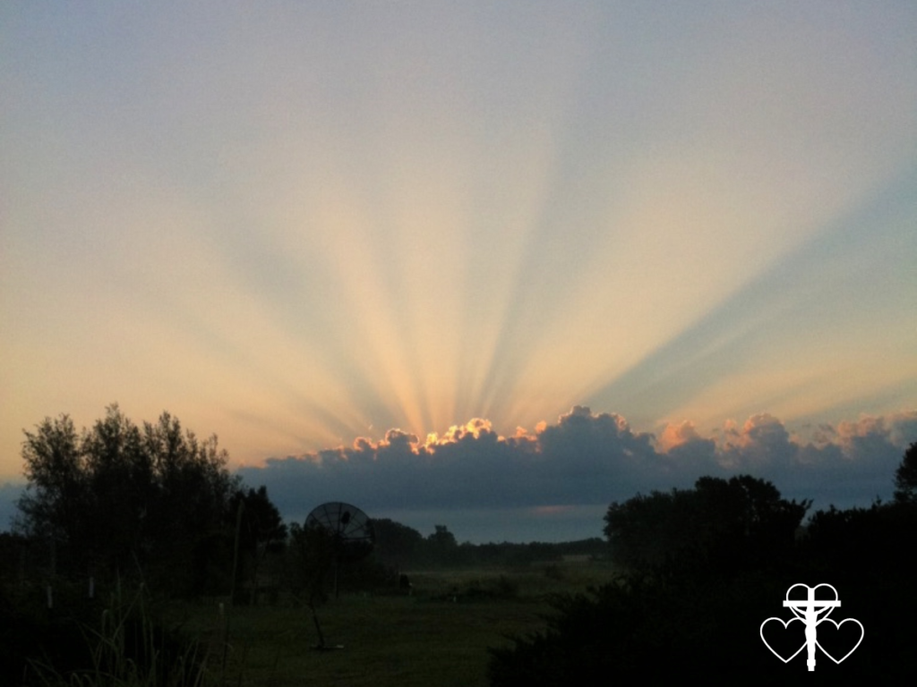 Picture of a sunset in the distance with light rays streaming up through the clouds.