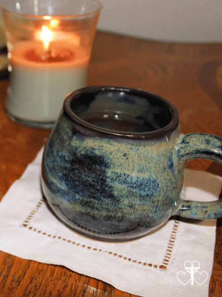 Picture of a burning candle and a mug of tea on a coaster sitting on a wooden table.