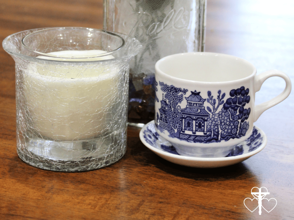 Picture of a blue and white china tea cup on a saucer, sitting next to a candle in a glass votive on a wooden table.