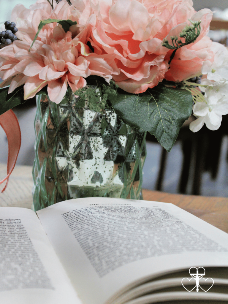 Picture of an open book with a flower bouquet in the background sitting on a wooden table.
