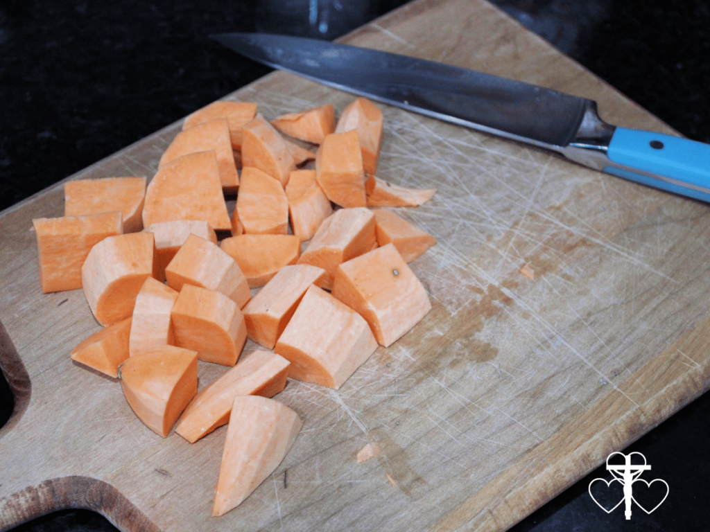 Picture of sweet potato cubes on a wood cutting board with a knife.